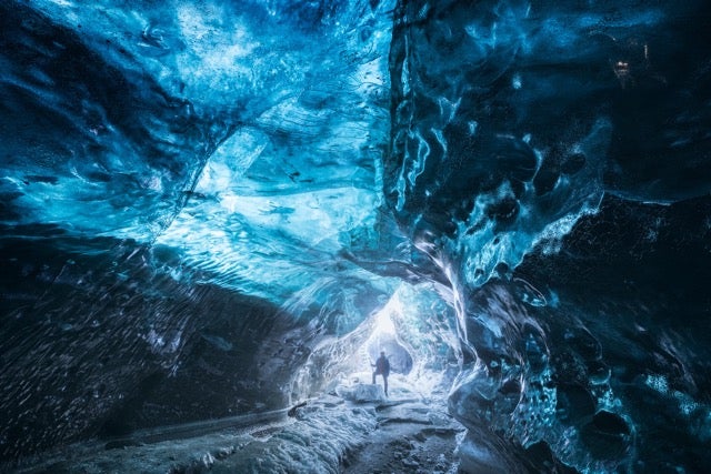 A caver stands at the end of the shimmering blue walls of Katla Ice Cave in the South Coast, one of the best day trips from Reykjavik in January. 