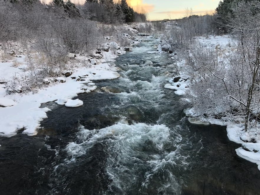 A river runs through a narrow path flanked by snowy fields in Ellidaardalur Valley in Reykjavik in January