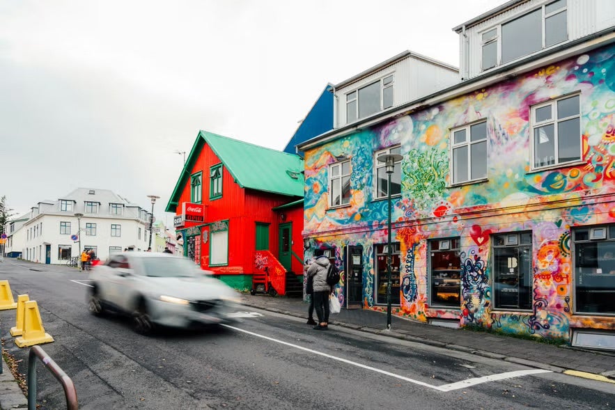 A car zooms past a building decorated with colorful art on its walls in Reykjavik. 
