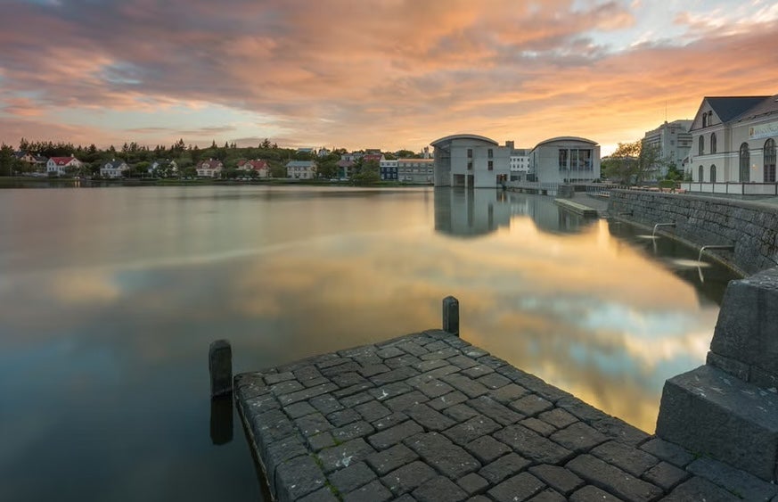 The pastel sky is reflected on the still waters of the Tjornin Pond in Reykjavik.