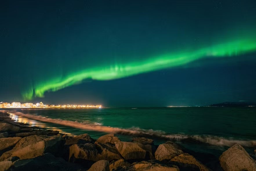 Bands of northern lights light up the harbor in Reykjavik on a winter night. 