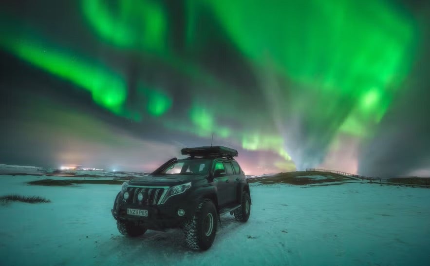 A car parked on a snowy spot with the northern lights dancing above. 