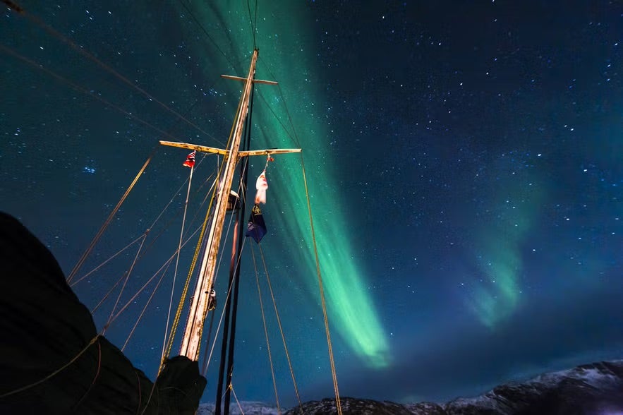 View of a mast of a boat with the northern lights in the background  on a northern lights cruise from Reykjavik.