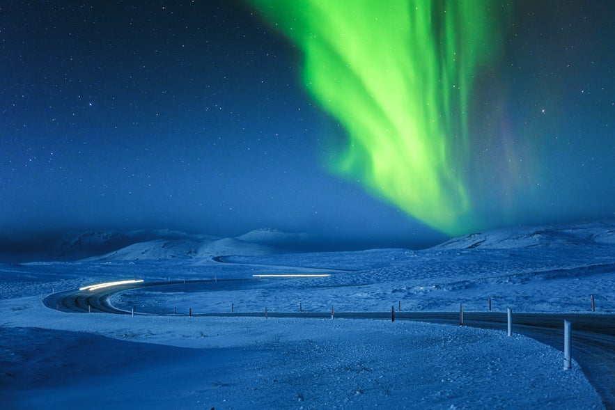 A stunning display of the aurora borealis dances over a road in Iceland, highlighting the natural beauty of the landscape.