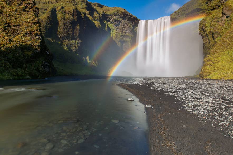 Regenboog boven het vallende water van de Skogafoss Waterval.
