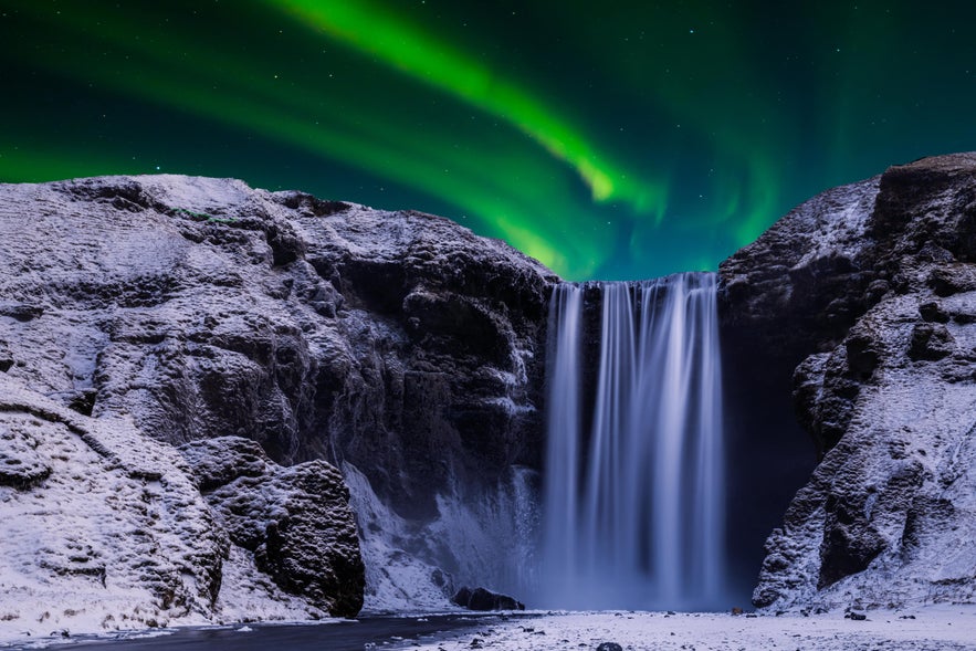 Skogafoss Waterfall illuminated under the northern lights in Iceland.