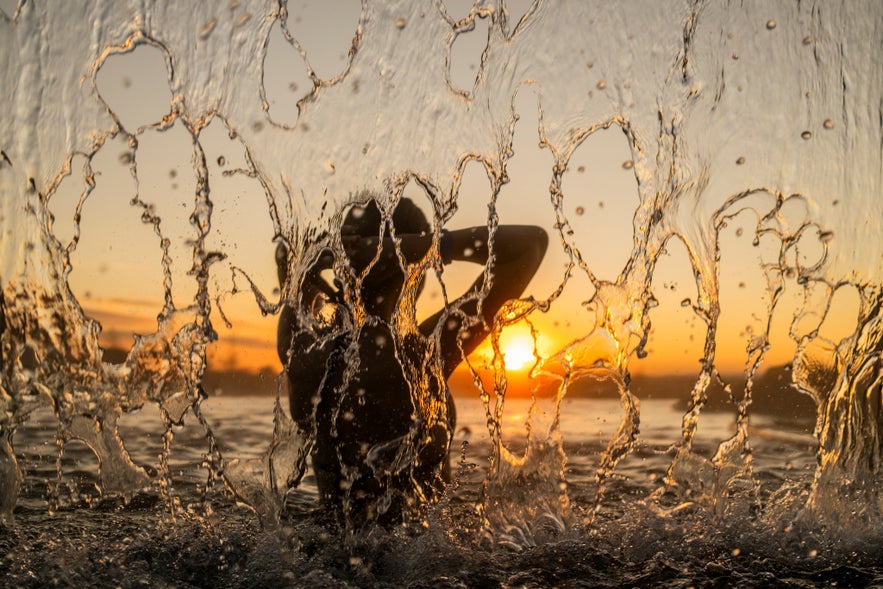 Guest enjoying the warm waterfall at Laugarás Lagoon in Iceland during sunset with golden light reflecting on the water