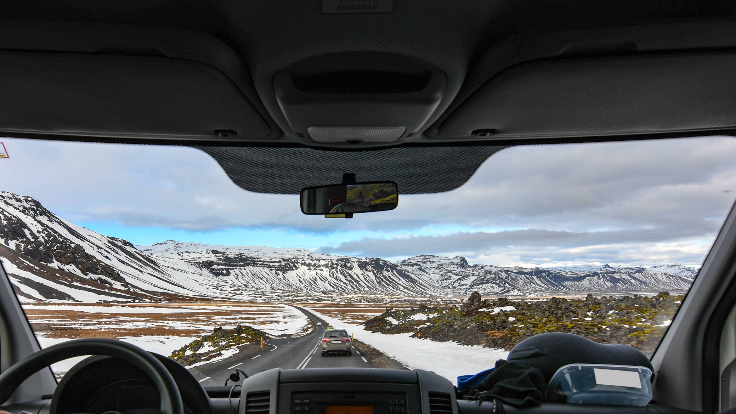 View from a car's interior where the dashboard is visible and snowy mountains are seen ahead on a private tour from Reykjavik.