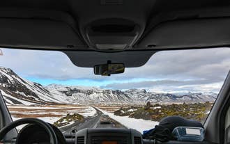 View from a car's interior where the dashboard is visible and snowy mountains are seen ahead on a private tour from Reykjavik.