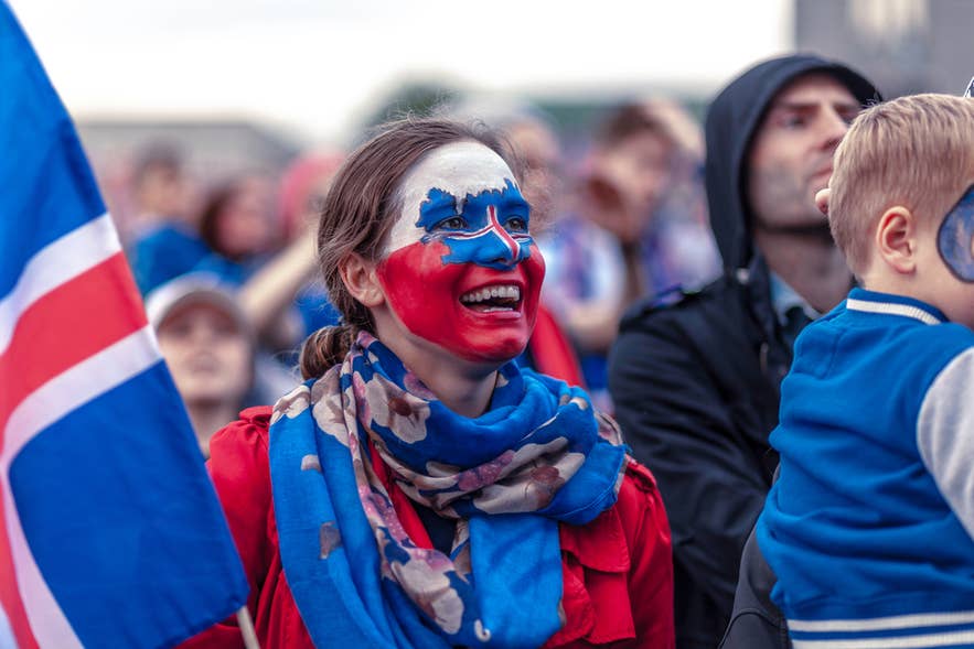 Donna con il volto dipinto con la bandiera islandese che sventola la bandiera nazionale durante le celebrazioni della Giornata dell’Indipendenza a Reykjavik.