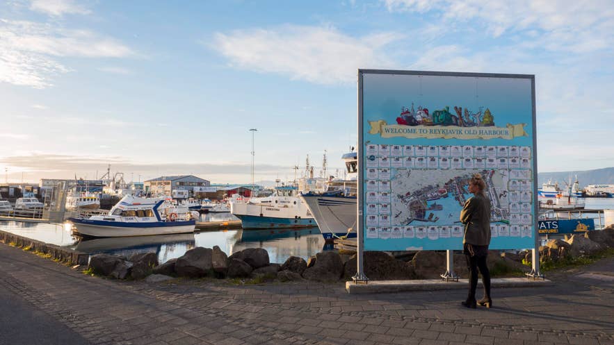 Donna davanti a una mappa al Vecchio Porto di Reykjavik, con barche ormeggiate sullo sfondo.