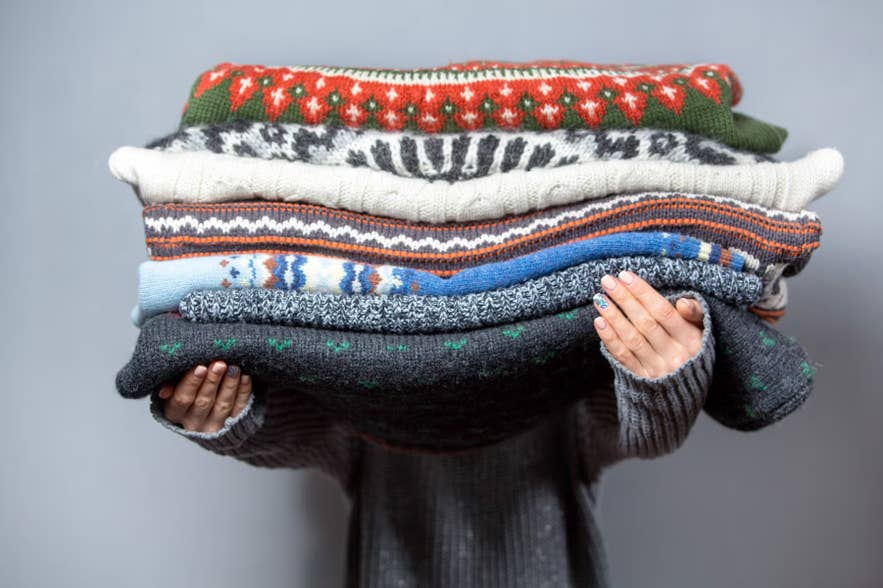 Person holding a stack of traditional Icelandic wool sweaters, known as lopapeysa, featuring colorful knitted patterns.