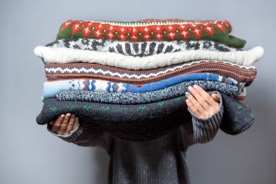 Person holding a stack of traditional Icelandic wool sweaters, known as lopapeysa, featuring colorful knitted patterns.