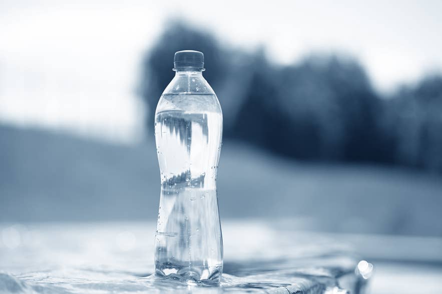 Clear plastic bottle filled with water placed on a reflective surface outdoors with a blurred background.