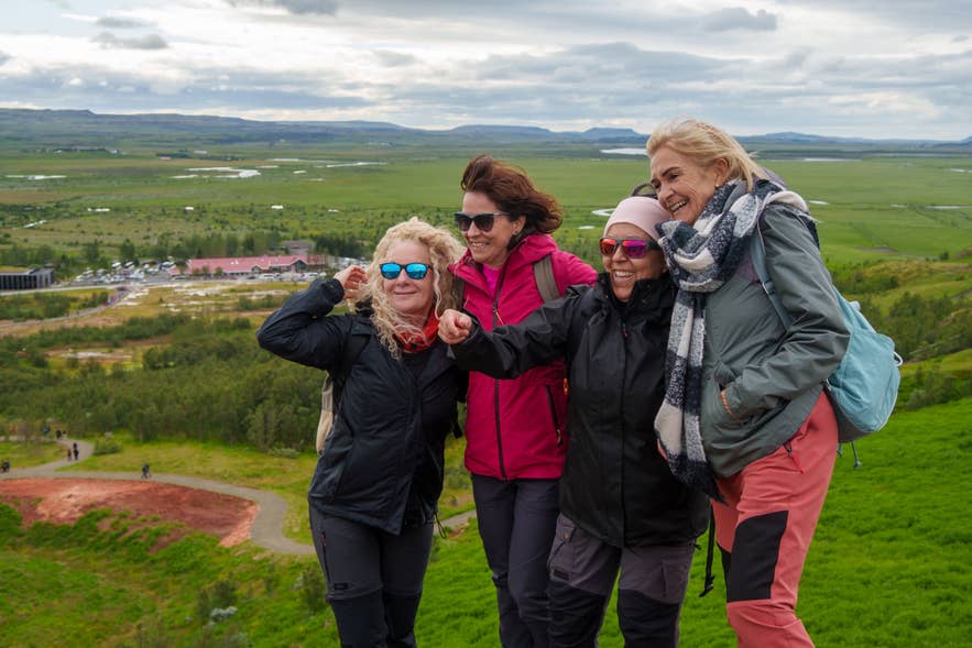 Group of four women enjoying a hike at Thingvellir National Park in Iceland, smiling with a scenic green valley and mountains in the background.