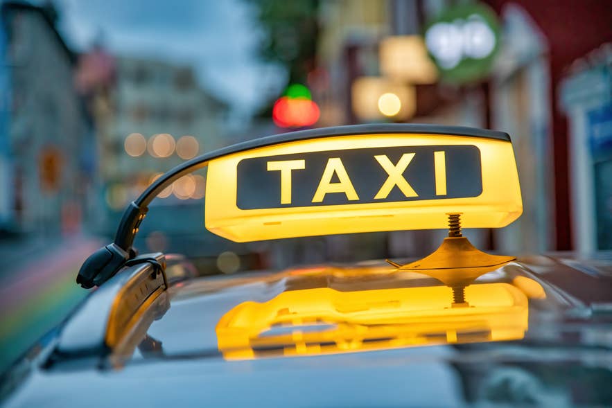 Yellow taxi sign glowing on top of a car in downtown Reykjavik, Iceland, with blurred city lights in the background.