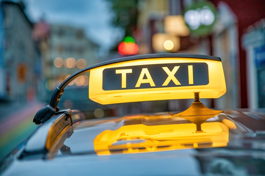 Yellow taxi sign glowing on top of a car in downtown Reykjavik, Iceland, with blurred city lights in the background.