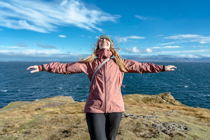 Traveler enjoying ocean views on an Iceland coastal cliff, showing why Iceland is worth visiting for nature and fresh air.