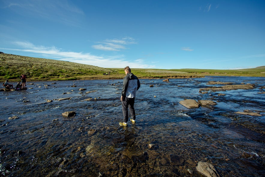 Traveler crossing a shallow river on the Glymur Waterfall in West Iceland.