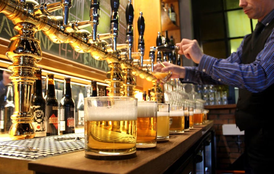 Bartender pouring beer from golden taps at a bar in Reykjavik, Iceland, with glasses of different brews lined up on the counter.