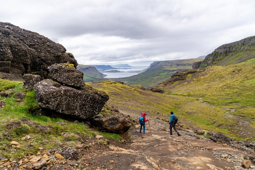 Hikers descending through mountain valley toward Hvalfjordur near Glymur Waterfall.