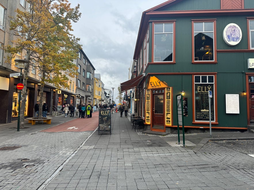 People walking along Laugavegur Street in downtown Reykjavik, Iceland, lined with colorful shops, cafés, and autumn trees.