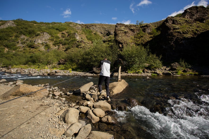 Hiker using a rope to cross the river on the Glymur Waterfall hiking trail.