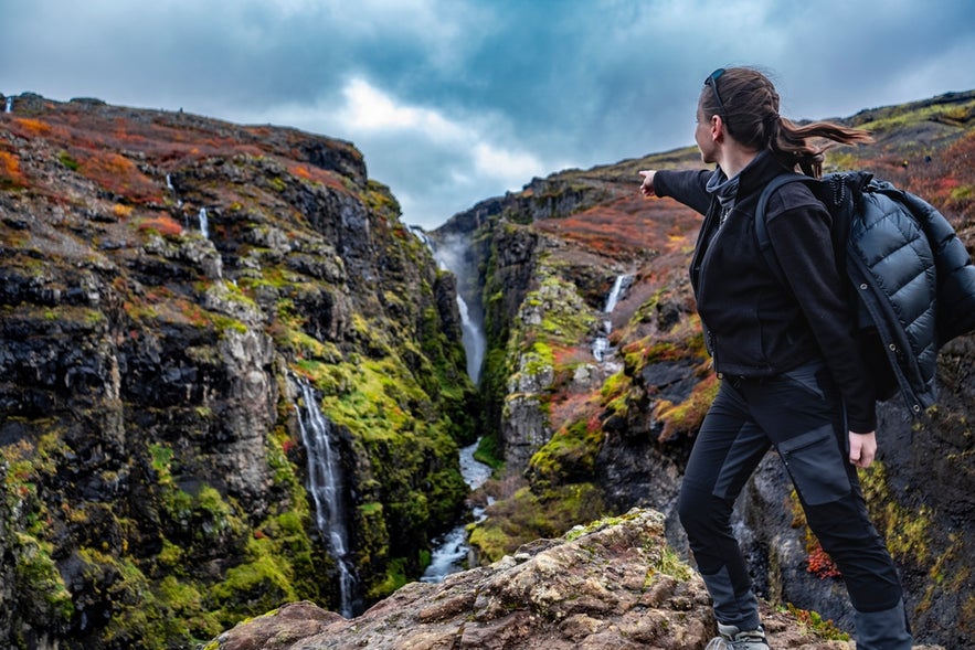 Hiker pointing toward Glymur Waterfall in the deep canyon of Hvalfjordur.