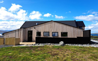Wooden Lonkot guesthouse in Iceland with black roofing set against a clear blue sky.