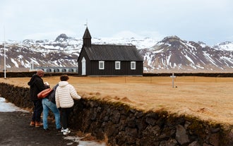 A family takes a photo of Budir Black Church with snowy mountains in the background.