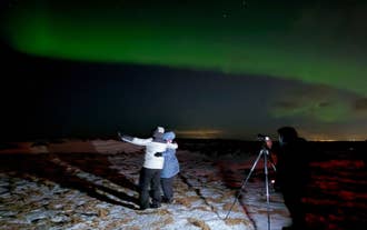 A couple poses for photo with their backs to the photographer on a northern lights tour in Iceland.