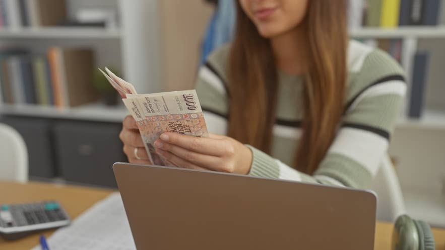 A person counting Icelandic krona banknotes at a laptop with a calculator on the desk. A person counting Icelandic krona banknotes at a laptop with a calculator on the desk.