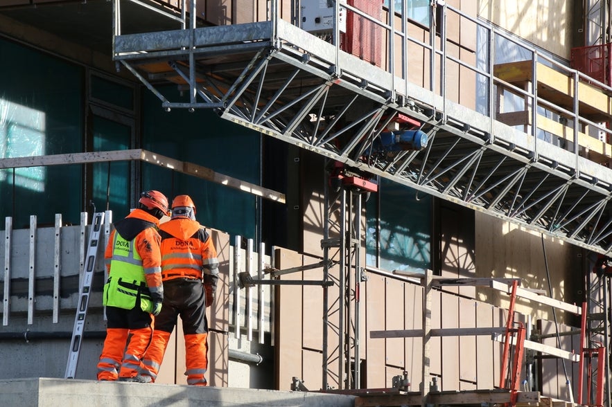 Two construction workers in safety gear on a building site for work in Iceland.