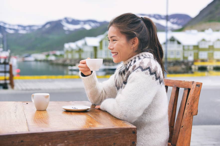 Donna con maglione islandese che si gode un caffè all’aperto, vivendo il febbraio islandese anche nel freddo