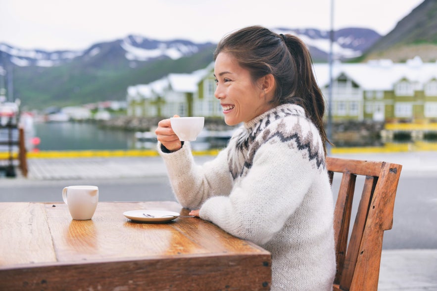 Woman in Icelandic wool sweater enjoying coffee outdoors, embracing February in Iceland's winter chill