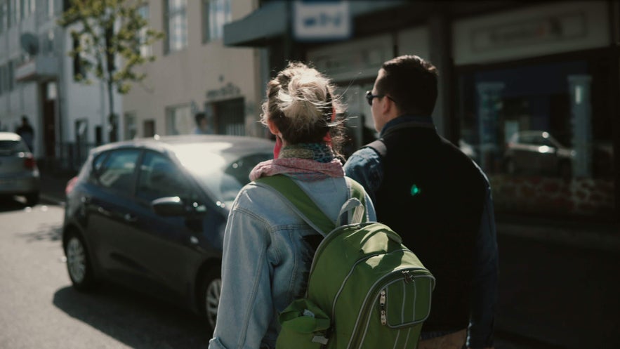 Two travelers walking through a sunny city street, enjoying the mild weather and long days of Reykjavik in May