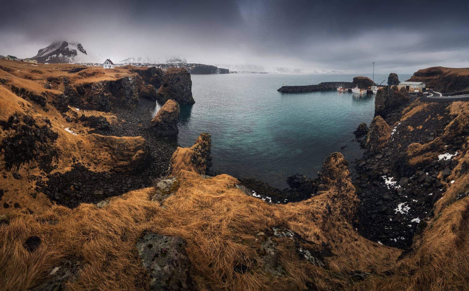 Arnarstapi’s snowy cliffs and turquoise water appear along a Snaefellsnes Peninsula tour.