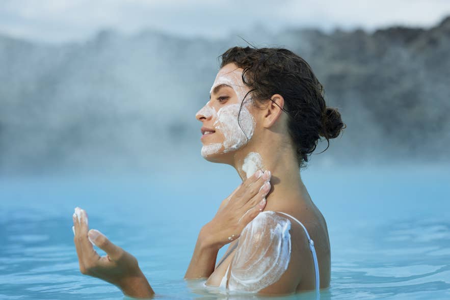 A woman applying a silica mud mask while relaxing in the Blue Lagoon