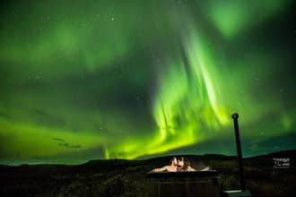 Couple relaxing in outdoor hot tub under northern lights near Fox Hostel in Hrifunes, South Iceland.