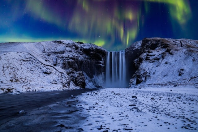Bands of purple and green aurora dance over the cascade of Skogafoss Waterfall, Iceland.