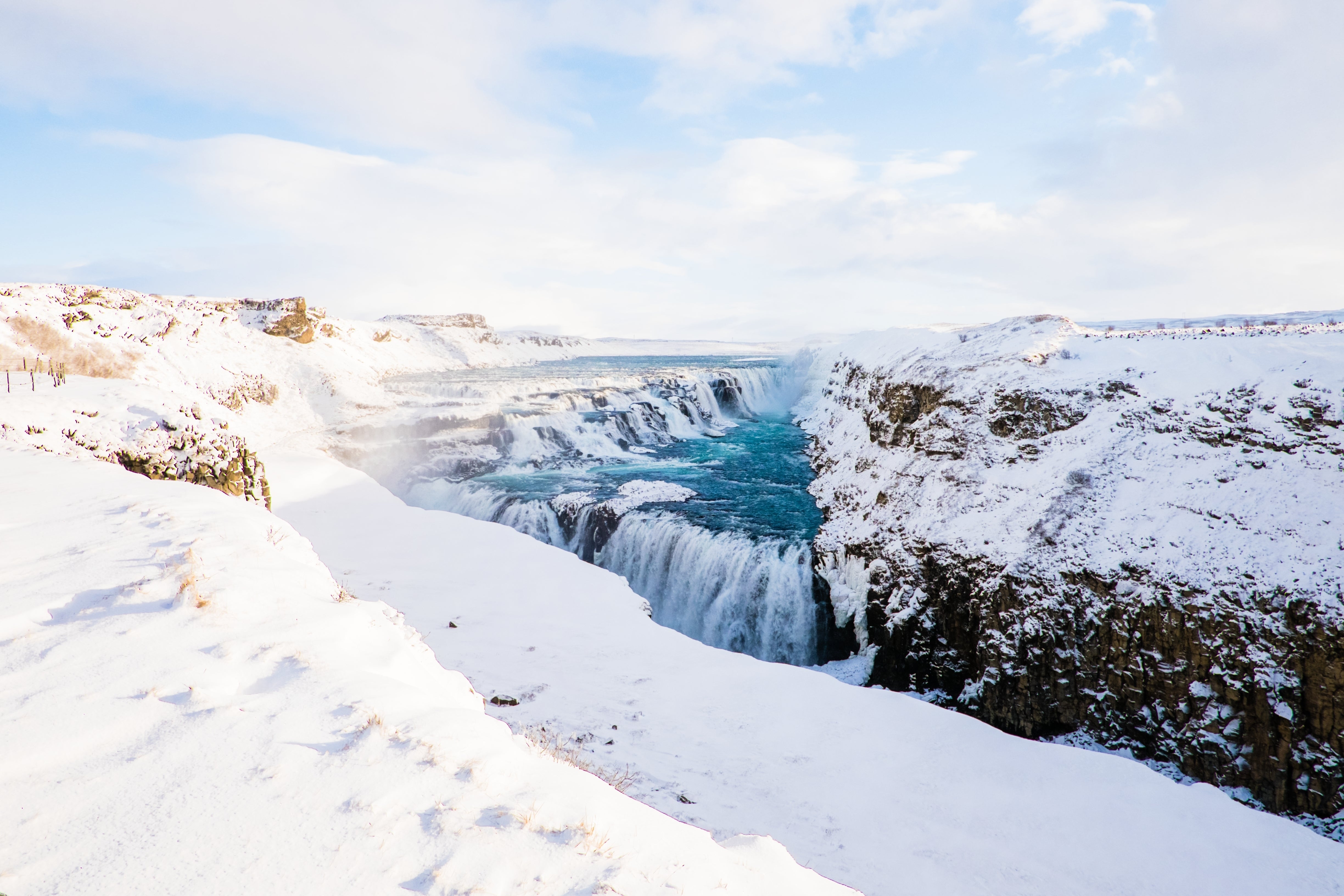 Snow-covered cliffs surrounding the turquoise cascades of Gullfoss waterfall on a bright winter day.