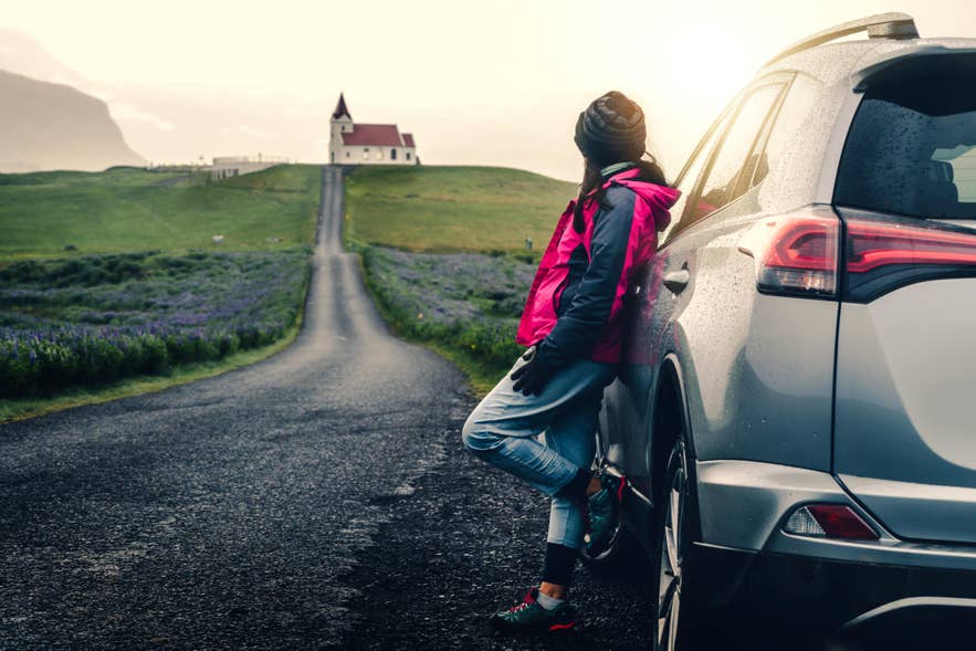 Woman on a self-drive tour in Iceland standing beside her car at a viewpoint.