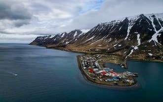 Luftfoto af en lille kystlandsby i Vestfjordene omgivet af stejle, sneklædte bjerge og fjorde.