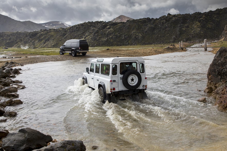 A 4x4 car crossing a shallow summer river in the Icelandic Highlands.