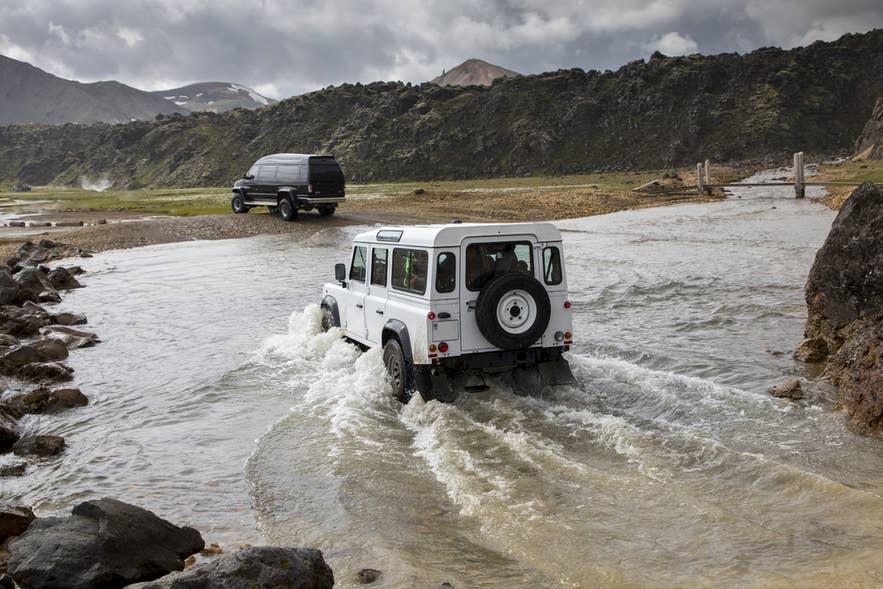 A 4x4 car crossing a shallow summer river in the Icelandic Highlands.