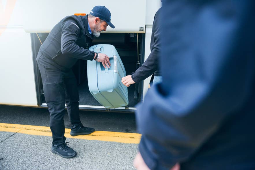 A driver of an airport bus transfer in Iceland places a piece of luggage in the bus compartment.