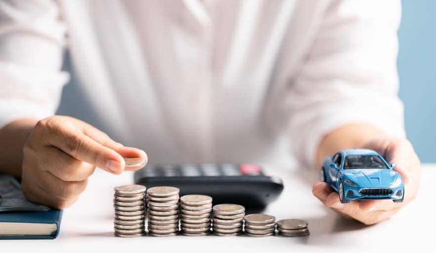 A man counts coins while considering the cost of an airport transfer in Iceland, with a miniature car and a blurred calculator in the background.