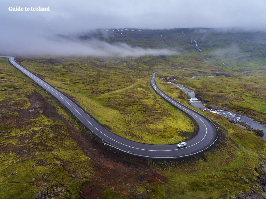 Car driving on a winding Ring Road stretch in misty mountains, a classic road trip scene in Iceland in April.