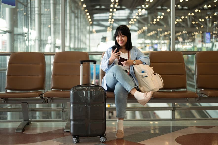 A woman sits at the airport while booking an airport transfer in Iceland.