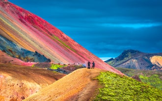 Colorful rhyolite slope with hikers walking along a bright red-and-yellow trail in Iceland's Laugavegur and Landmannalaugar.